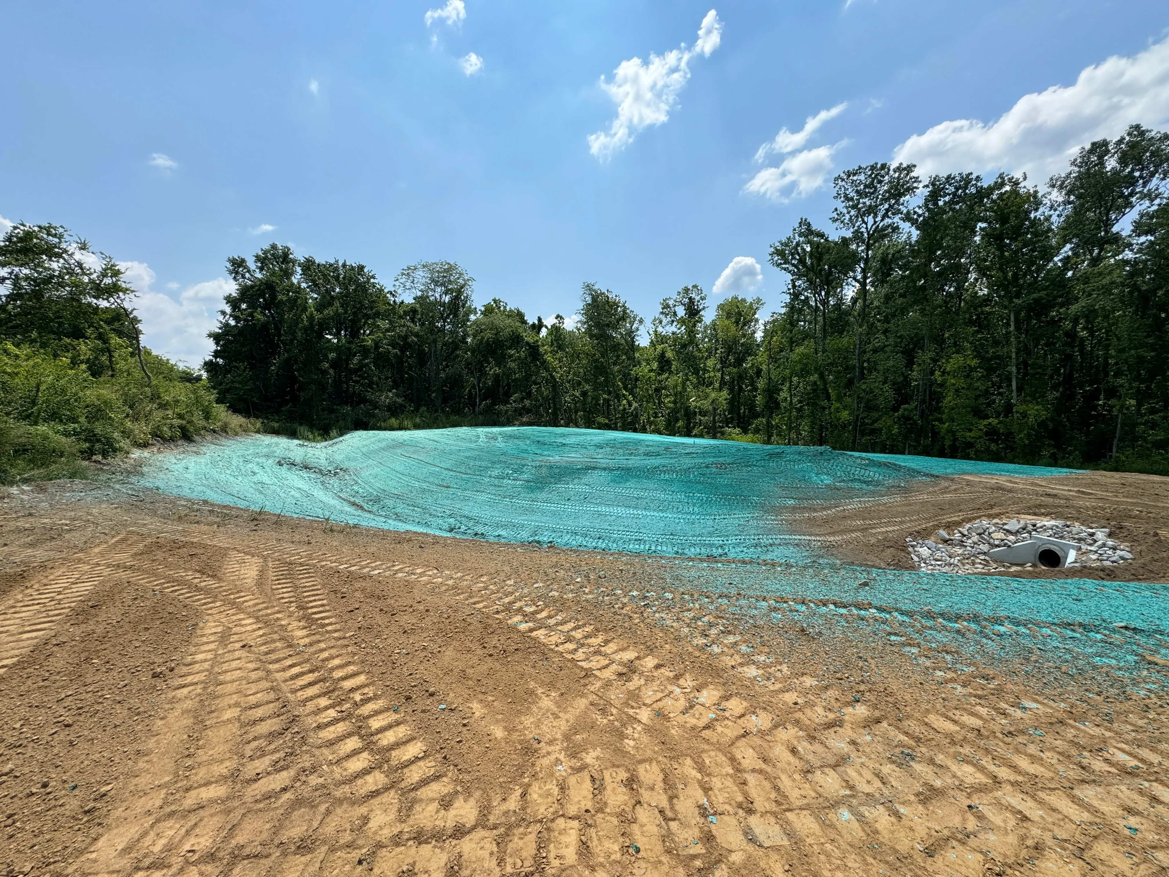 Turquoise erosion control netting on graded soil with drainage pipe and aggregate base