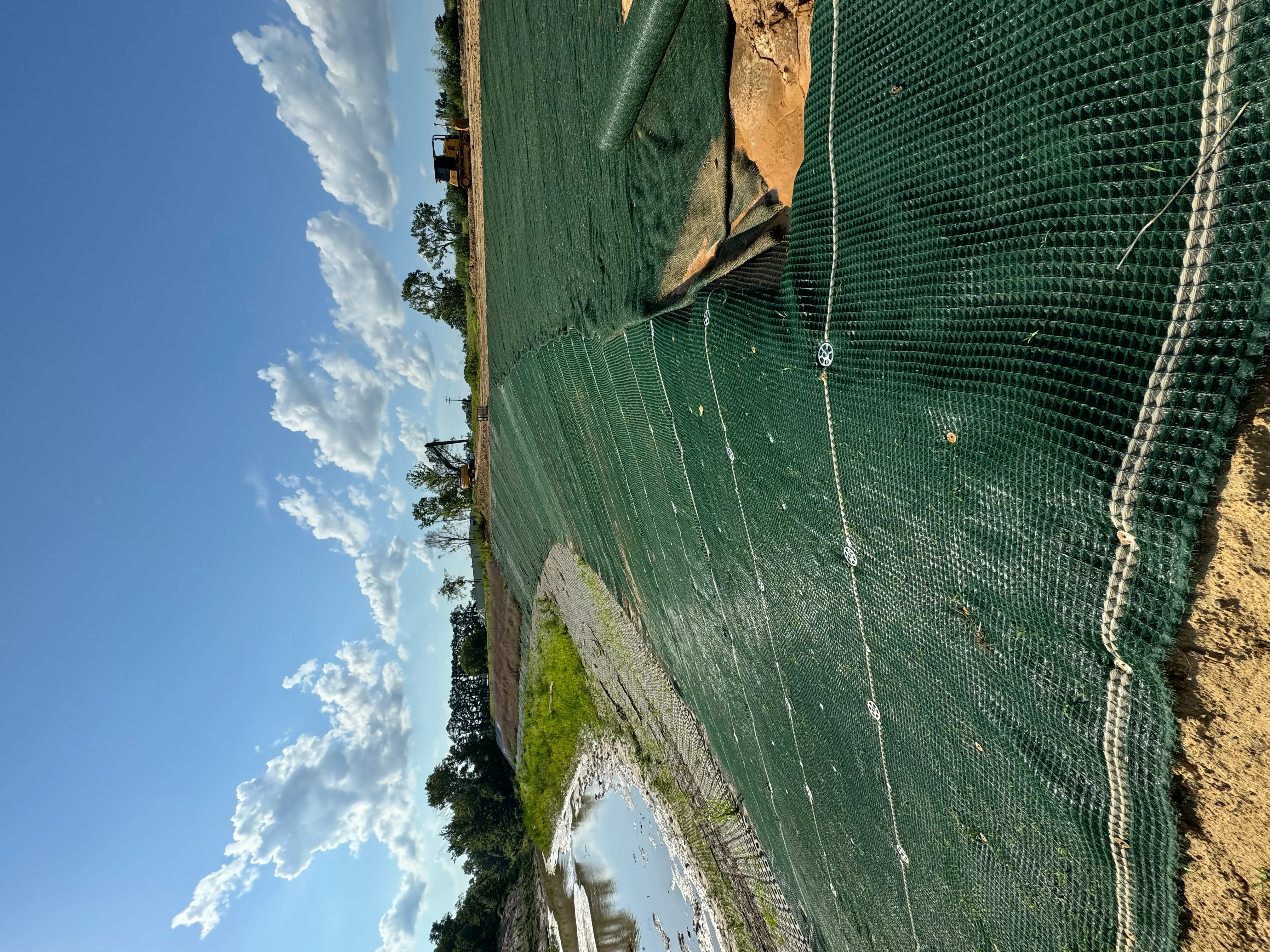 Green erosion control netting installed on sloped earthwork with stakes and cable securing