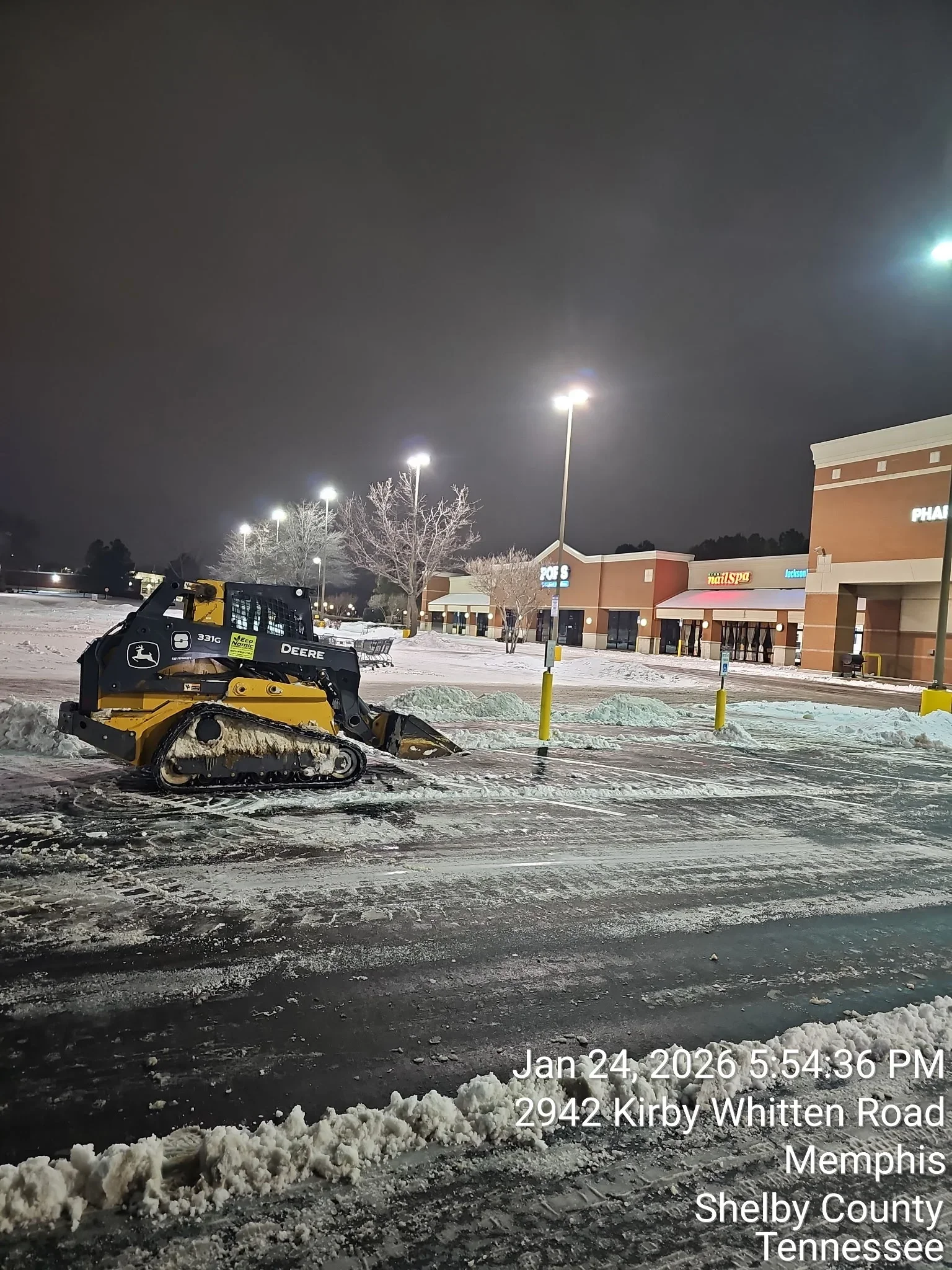 John Deere track loader removing snow from commercial parking lot at night