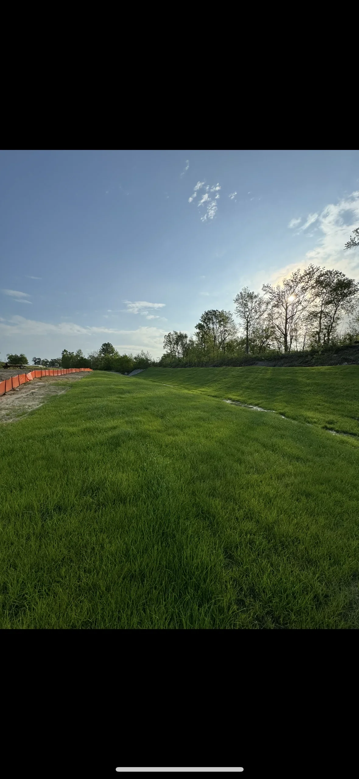 Orange silt fence erosion control barrier along seeded grass area with drainage swale