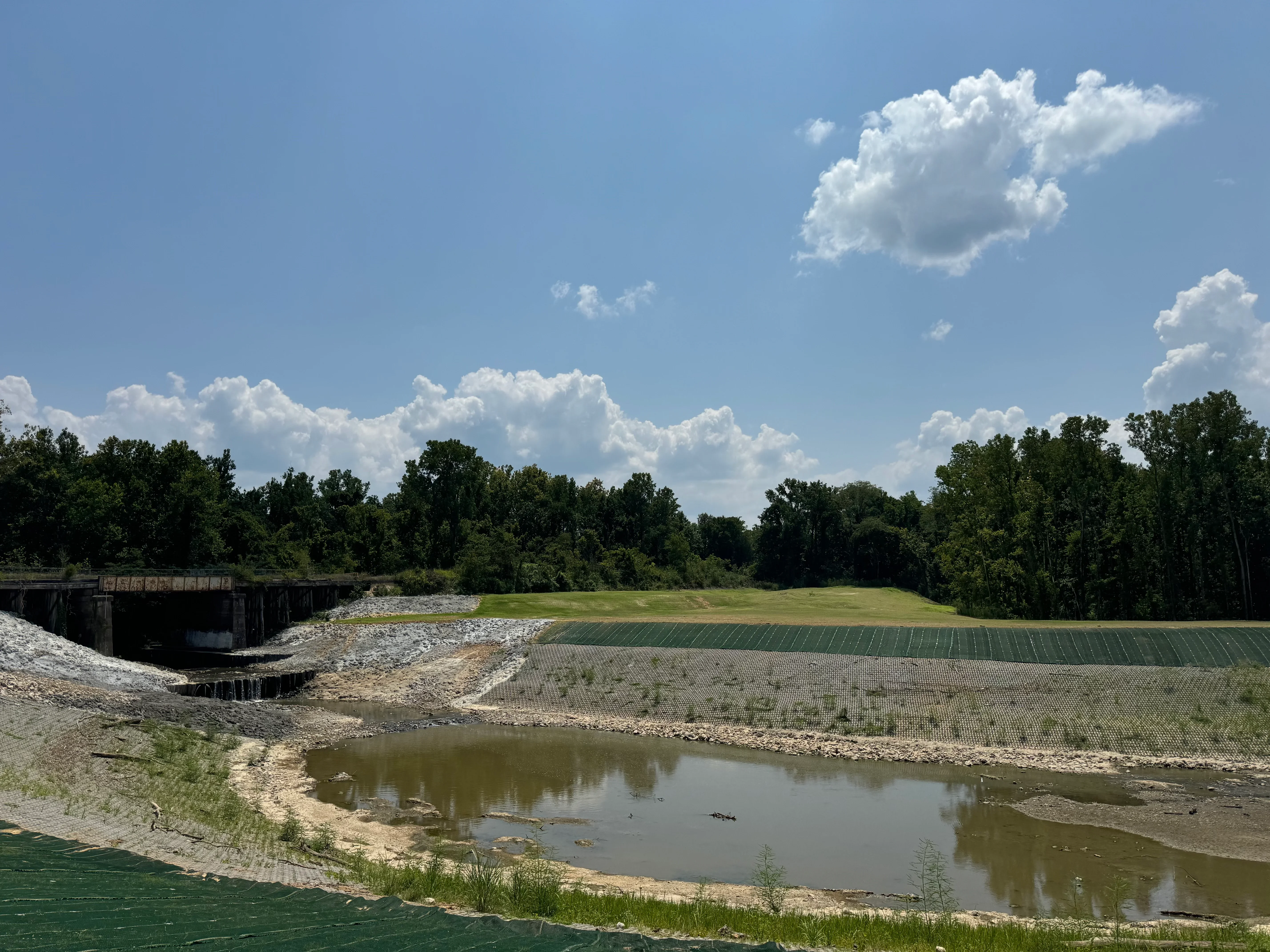 Riprap and gravel erosion control installation along stream with agricultural fields and tree line