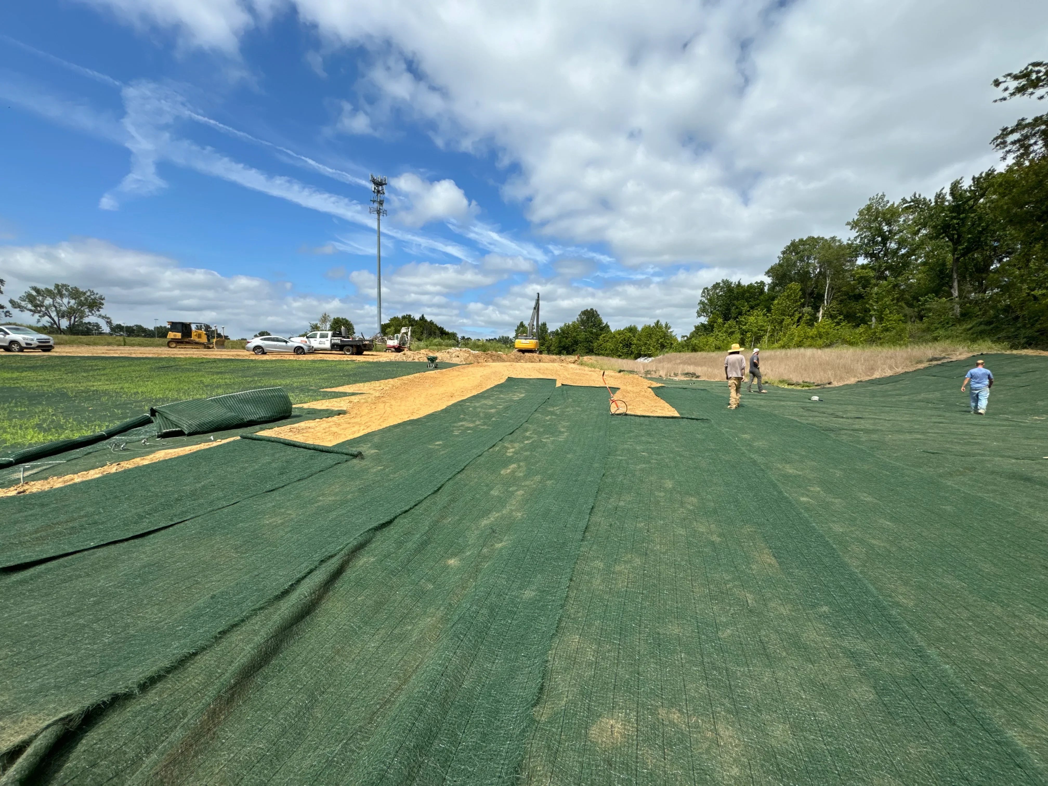 Green erosion control matting installed over prepared soil with straw base layer on large site