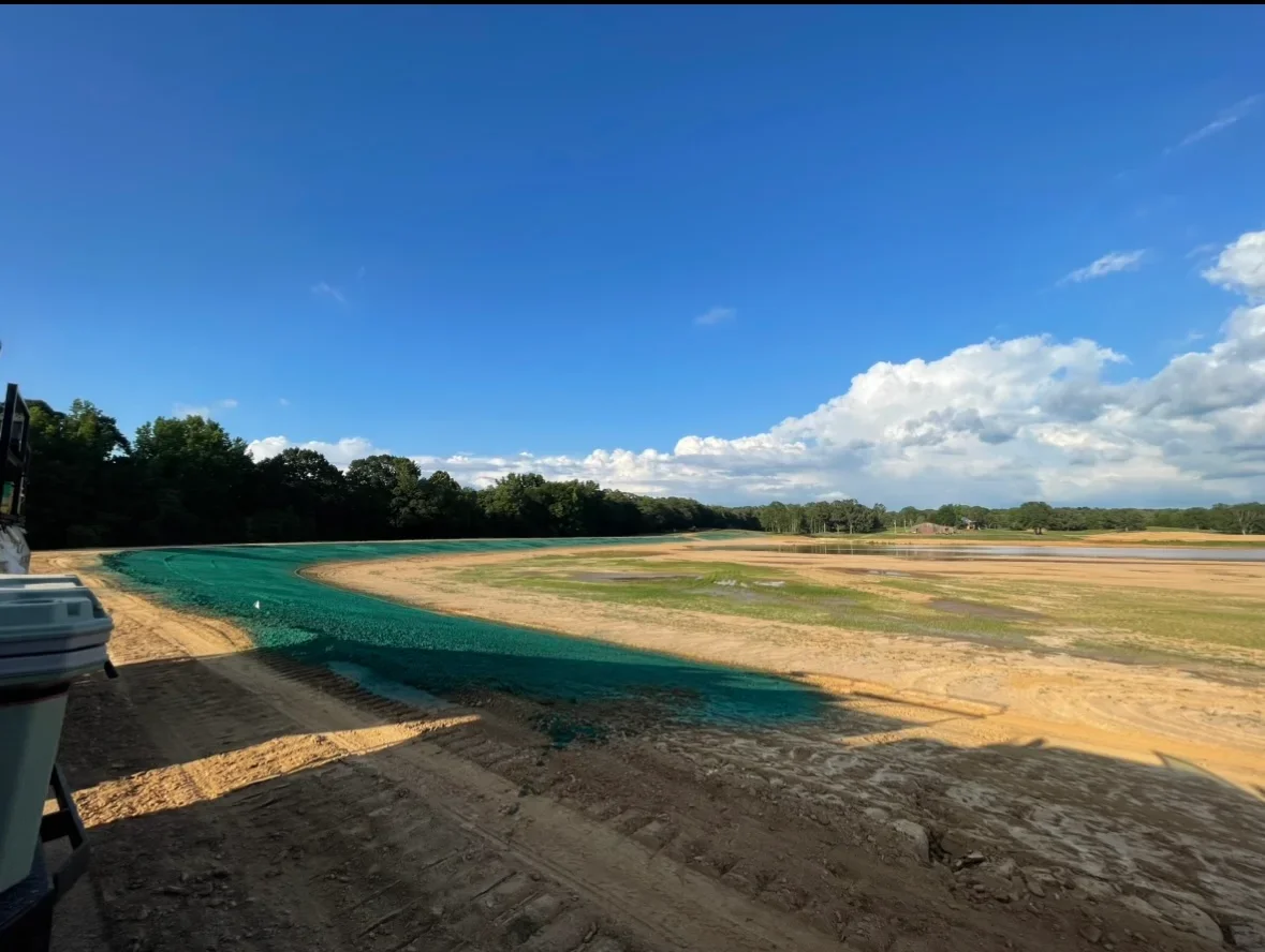 Turquoise erosion control matting installed along waterway banks with sandy soil stabilization